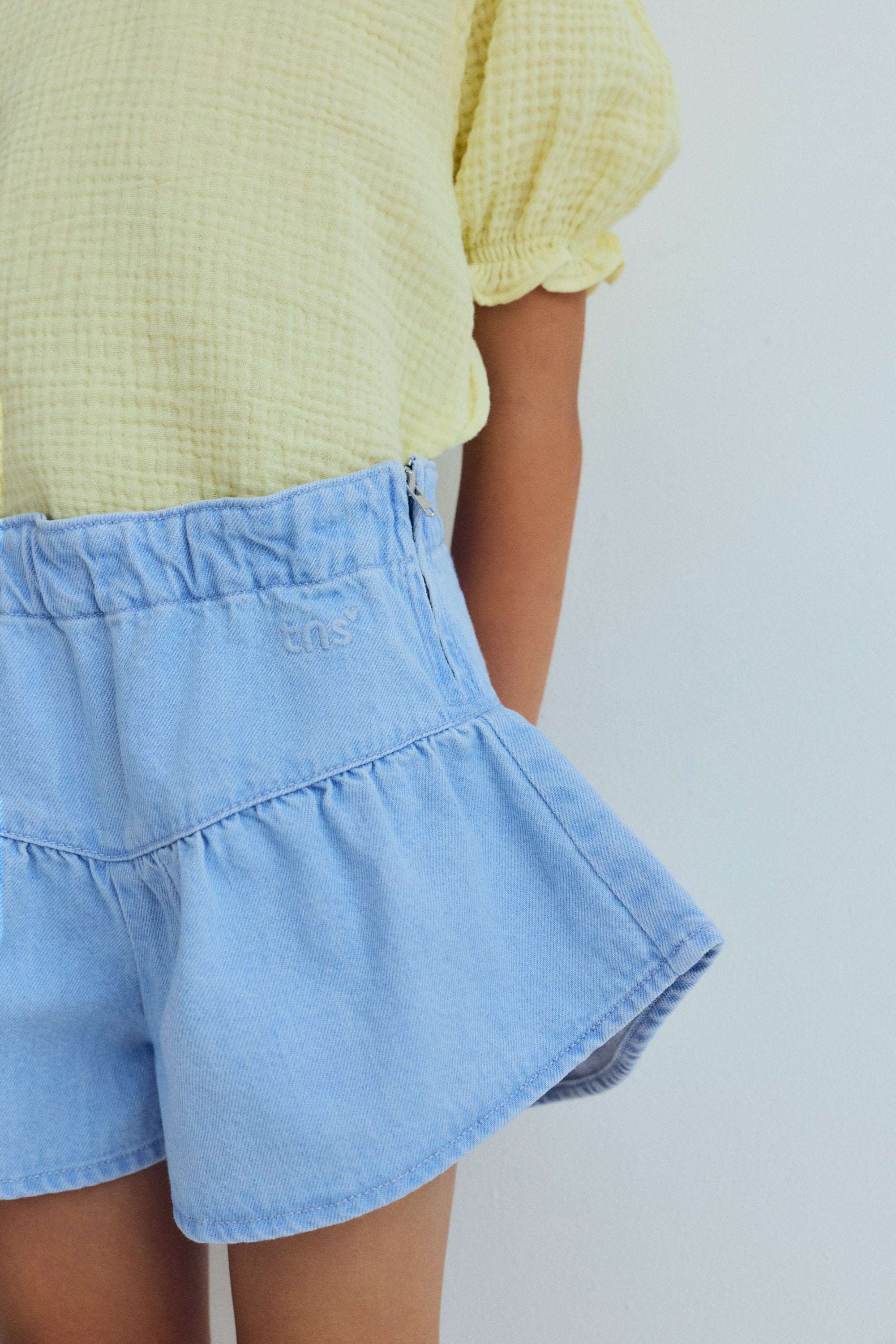 Washed denim shorts with a pointed cut and voluminous leg, featuring delicate ruching for a fresh, playful silhouette.