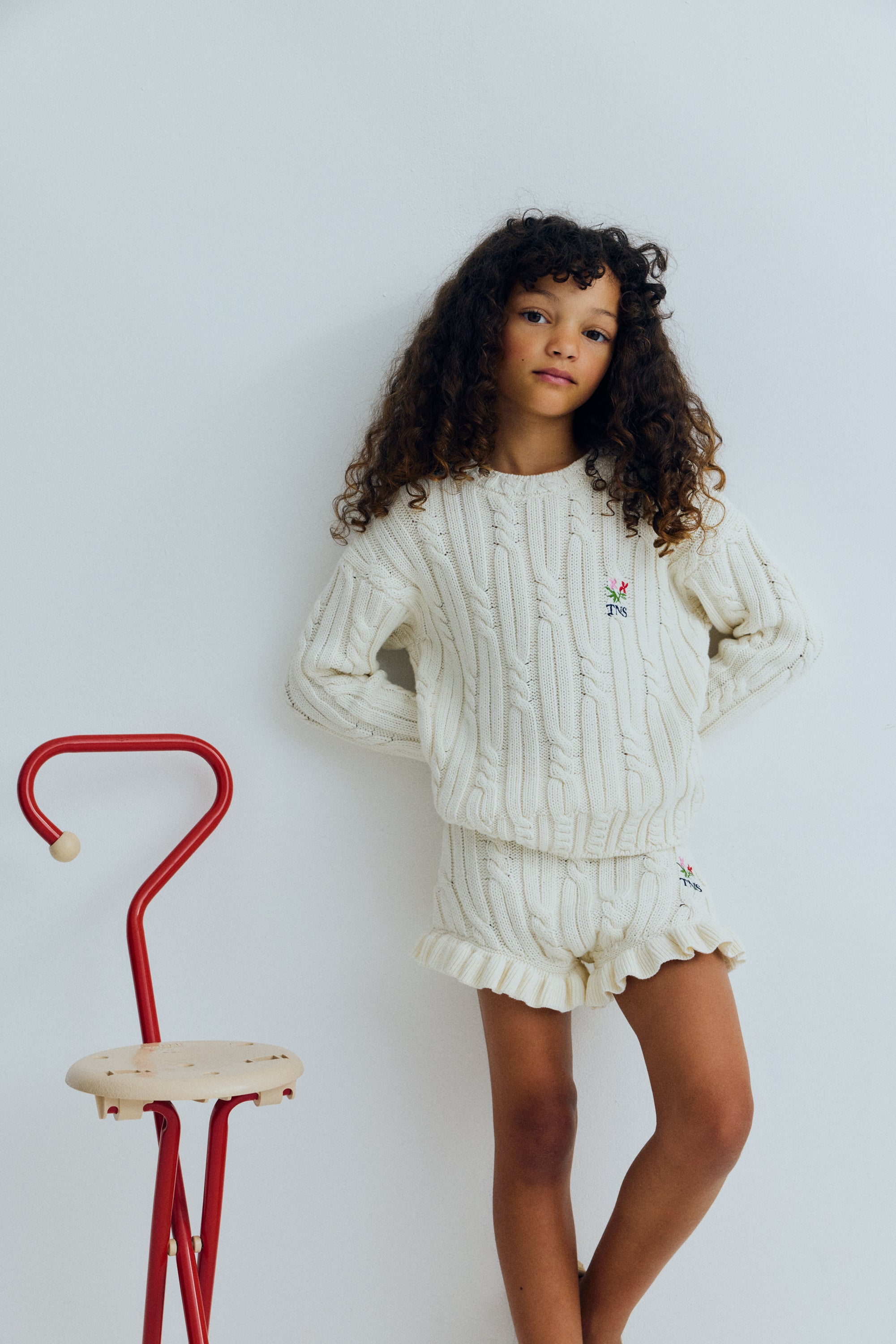 Cable knit sweater with&nbsp;subtle cable details on the collar, cuffs, and hem, featuring a playful floral branded embroidery on the chest.