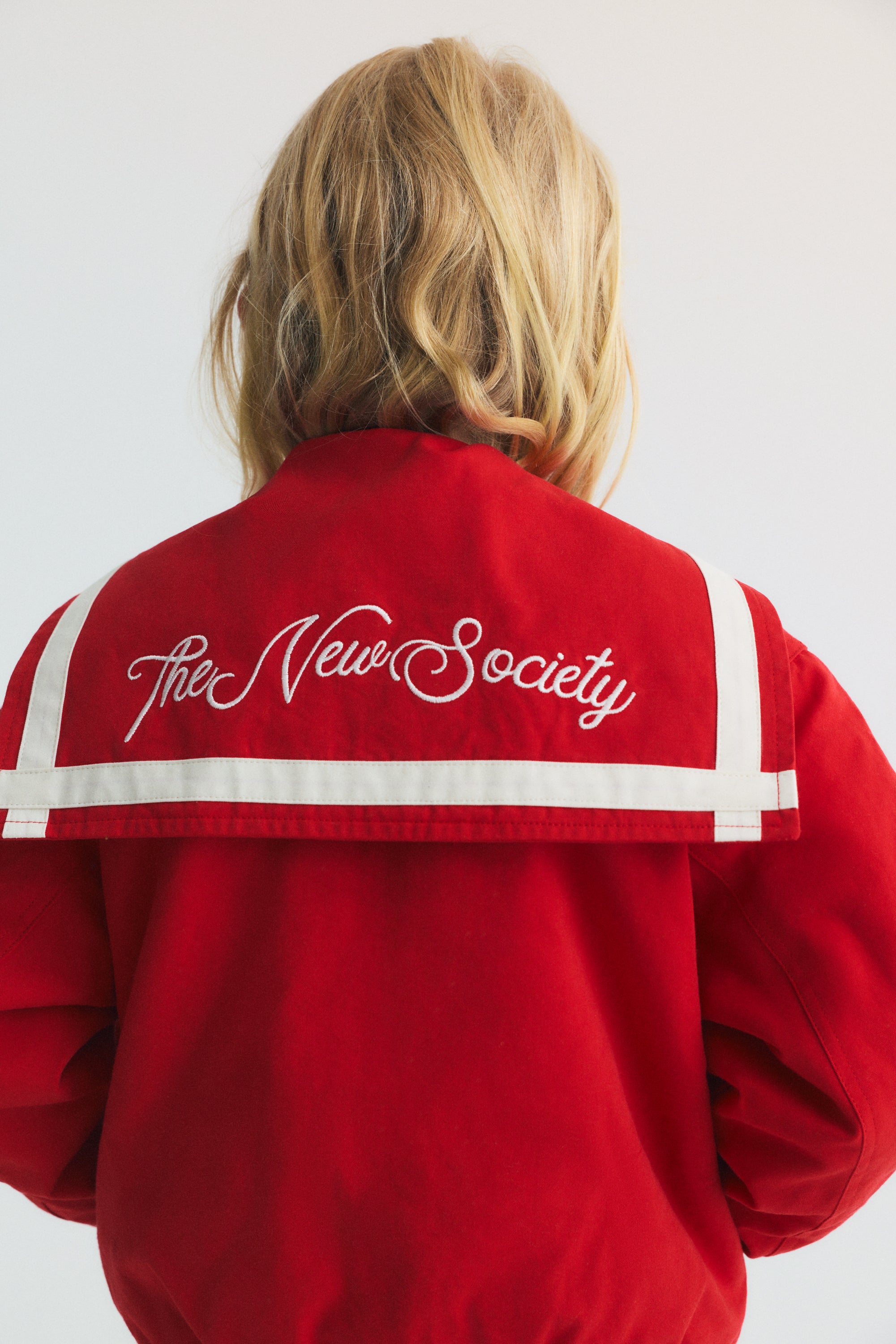 Bomber style jacket in a&nbsp;vibrant red, featuring a unique sailor collar, embroidered Society logo on the back, and contrasting stripes. 