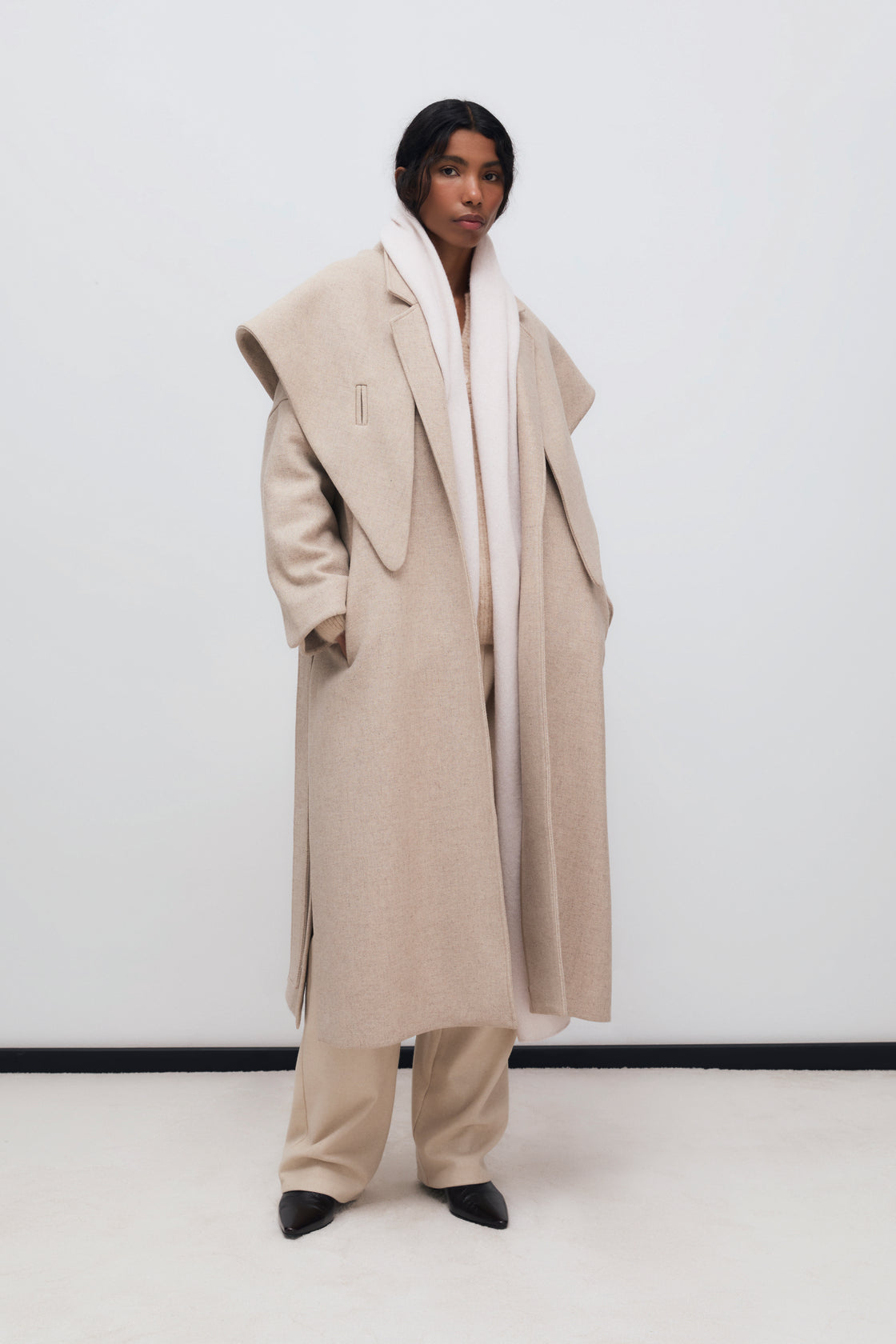 Long wool coat with lapels and side slits. It is double-breasted with a matching fabric belt. It comes with a scarf made from the same fabric.