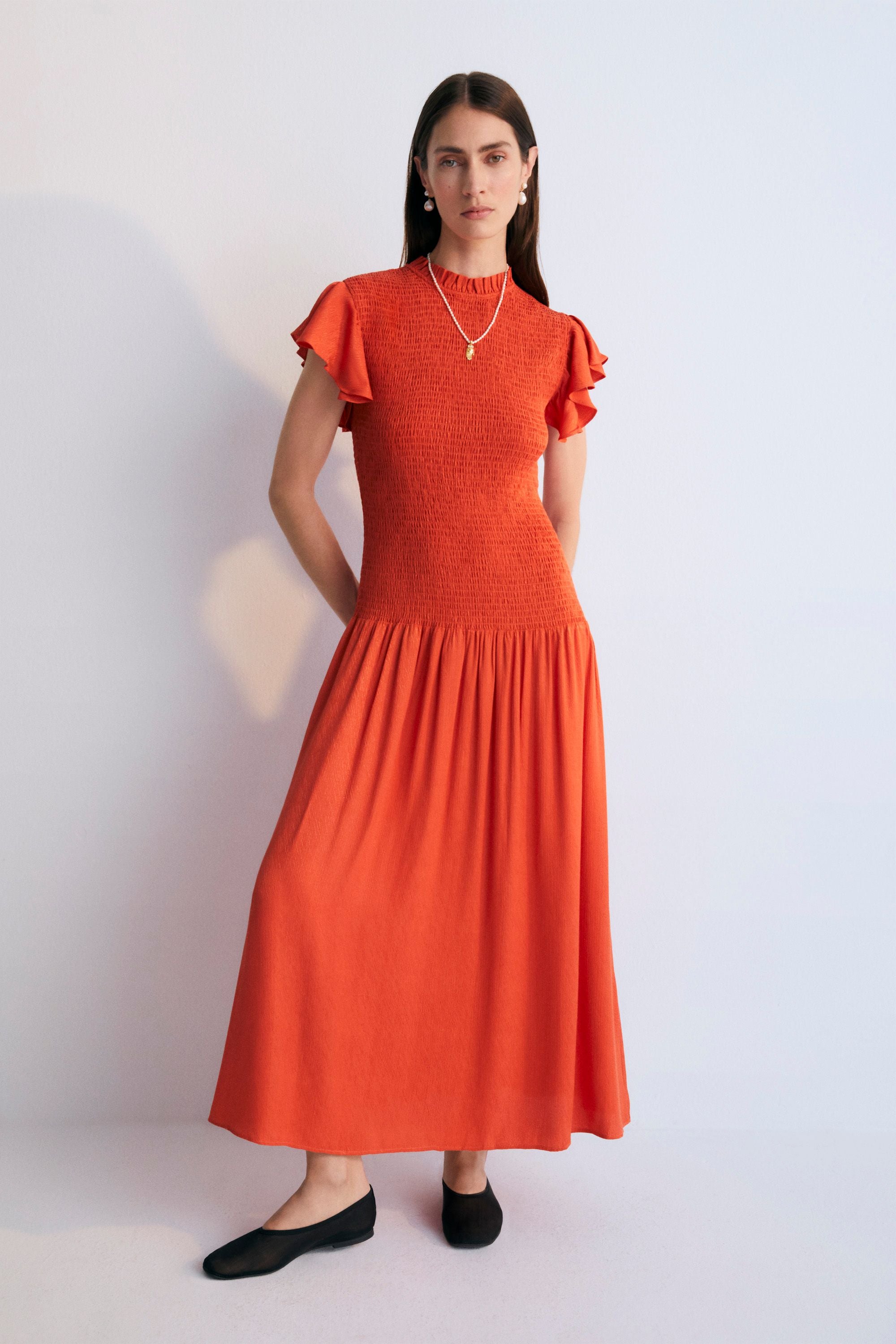 Long jacquard-woven dress in a lovely chili color with smocking on the bodice and ruffles on the shoulders. Spring Summer Collection. The New Society.