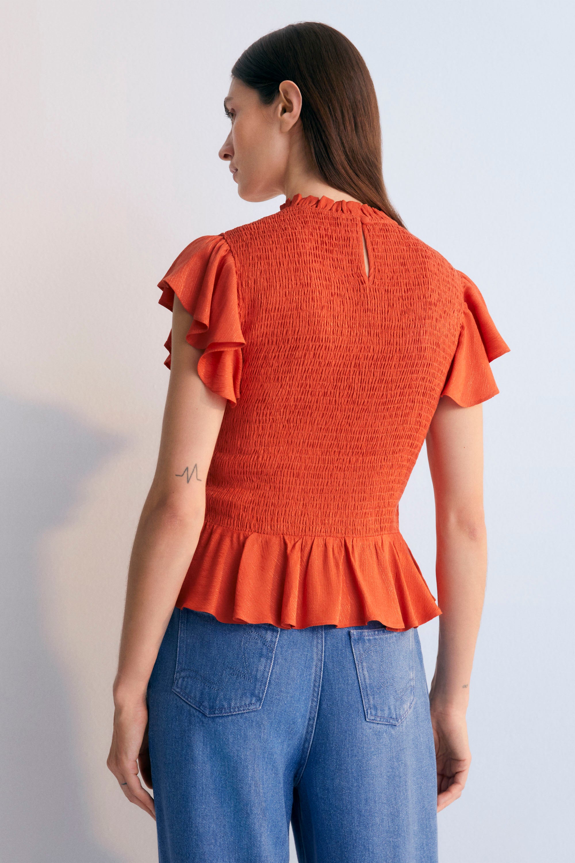 Jacquard woven blouse in a lovely chili color with smocking on the body and ruffles at the waist and shoulders.