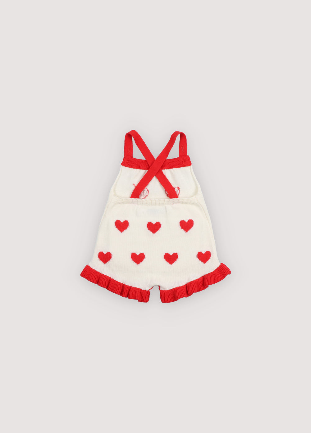Fine cotton knit romper featuring playful heart jacquard, buttoned side slits with mother of pearl buttons, a contrasting ruffle hem, and adjustable crossed straps at the back for a cute, comfortable fit.