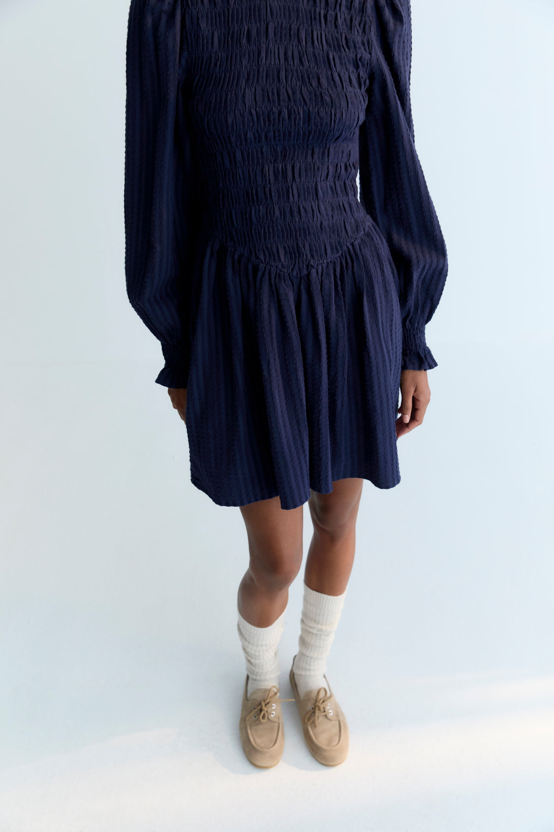Short seersucker dress with a smocked bodice and V-shaped finish. It features puffed sleeves and a round neckline with a ruffle detail.