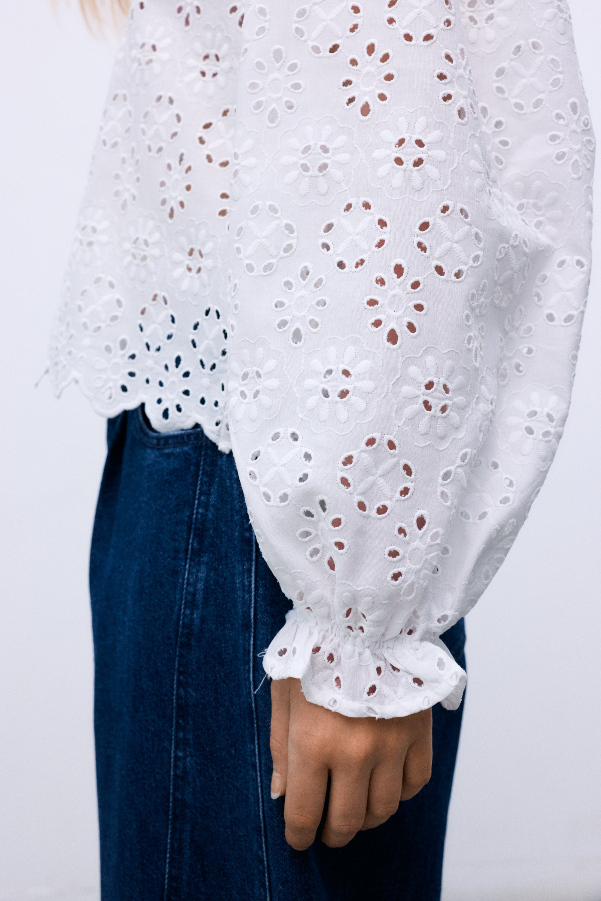 Confectionné dans un magnifique 100 % coton avec une broderie exquise, ce chemisier présente des manches volumineuses terminées par des poignets élastiques et un volant délicat.