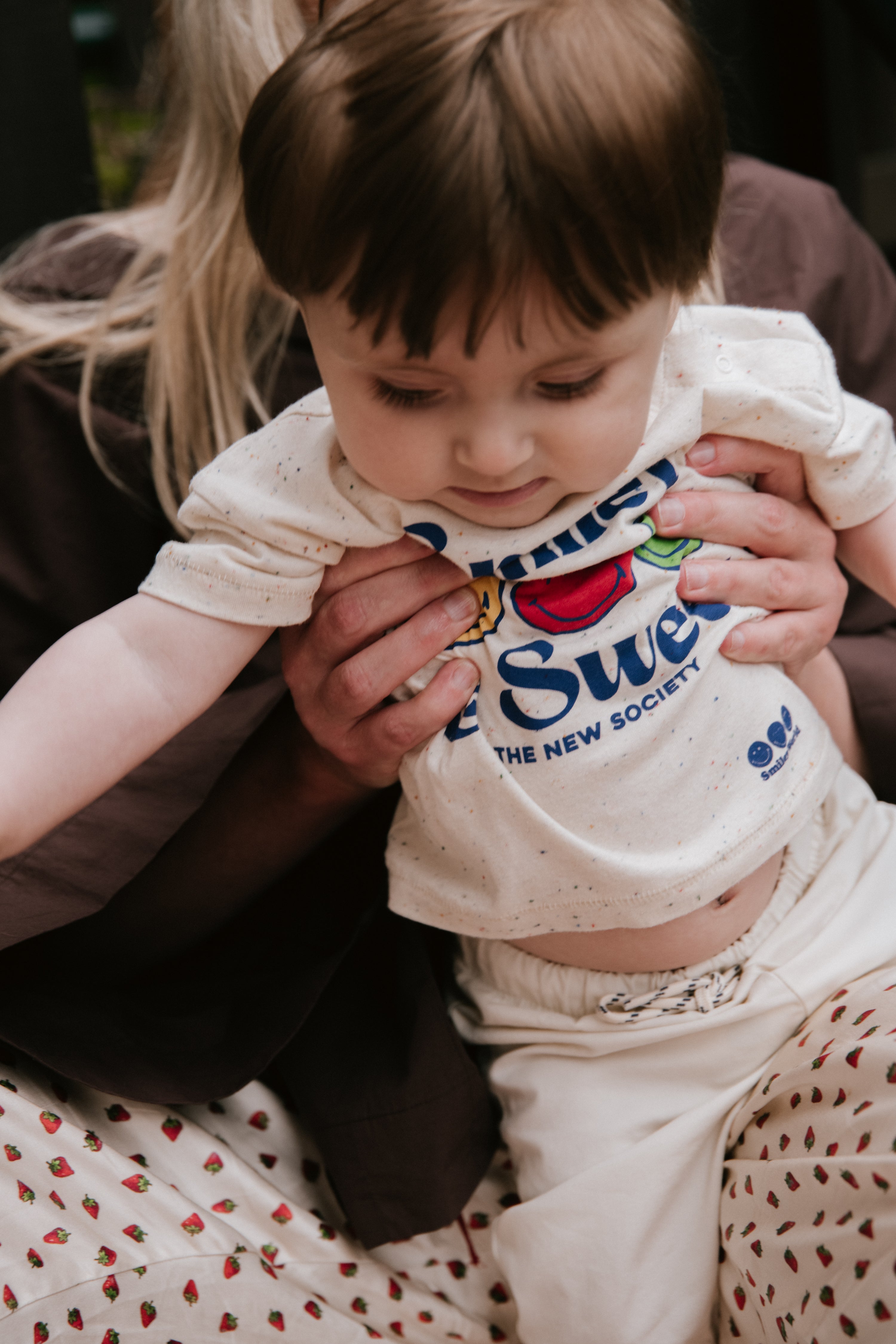 Fun speckled jersey T-shirt featuring a SmileyWorld® print on the front and shoulder snaps for easy wear, adding a playful, practical touch.