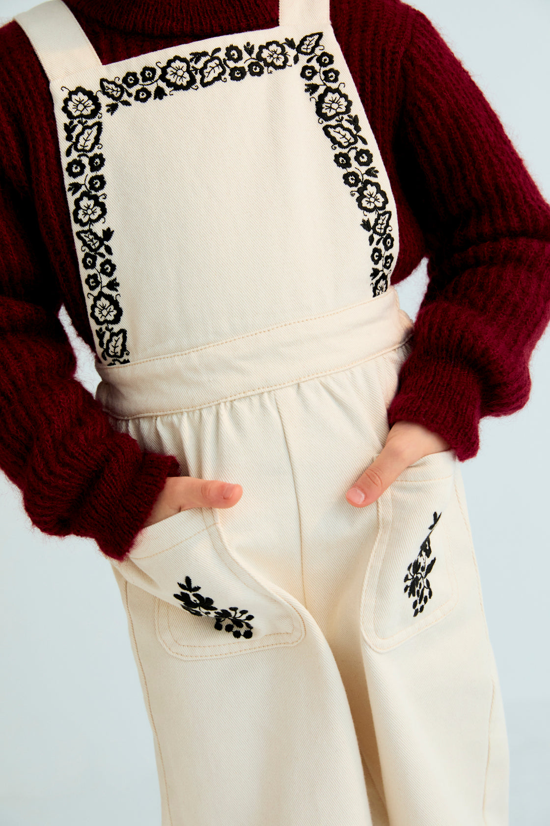 Denim overall with contrast embroidery details on the upper front and two patch pockets in the front. It features an elastic waistband at the back and adjustable straps at the back.