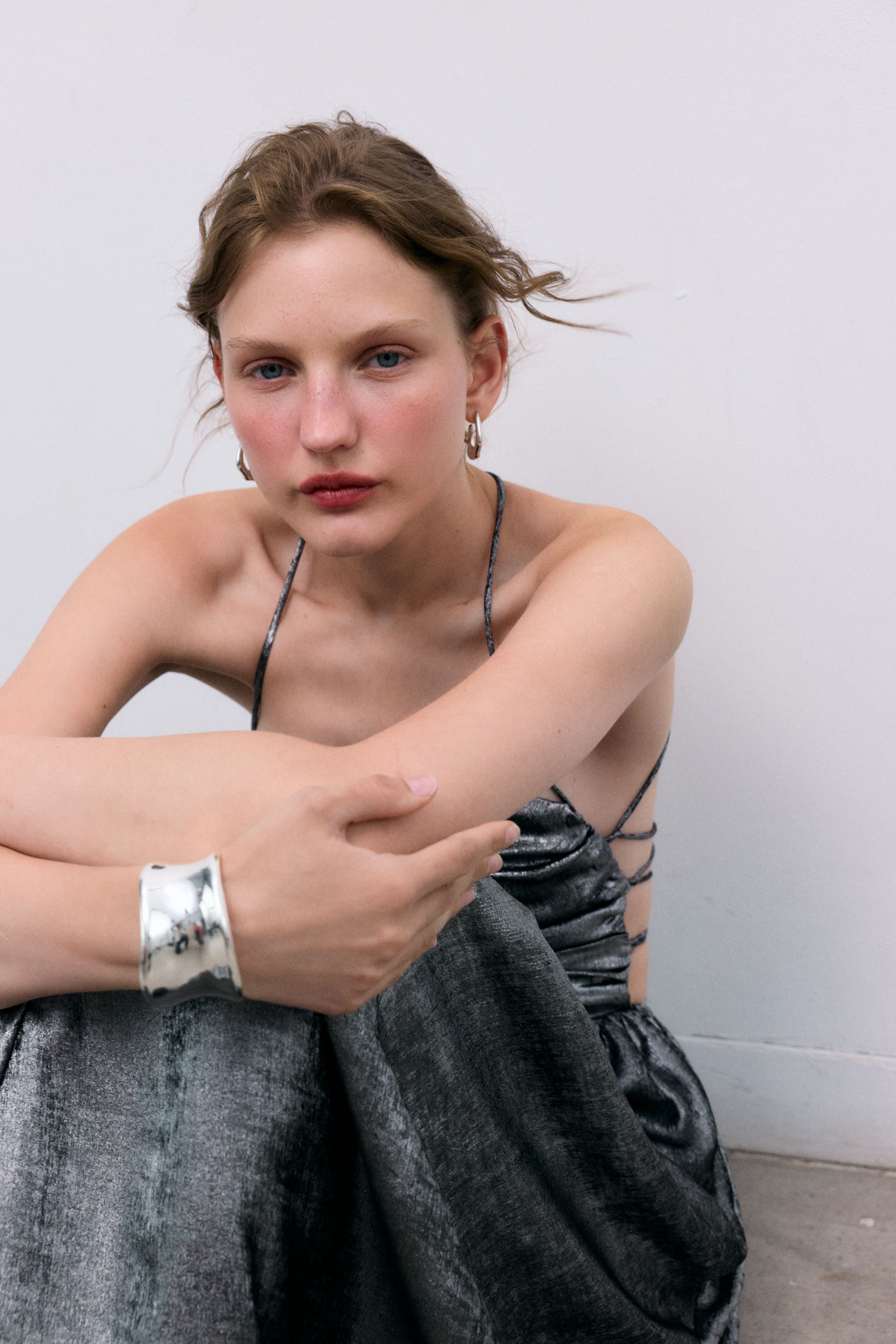 Silver shine dress with a waist cut and front ruching. It features spaghetti straps that cross at the back and a zipper closure.