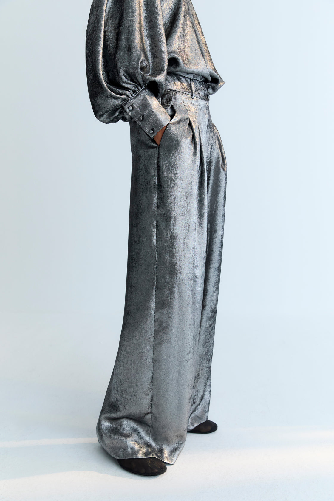 Straight pants in silver shine fabric with front pleat detailing, pockets, and a crossover waistband with a hidden button.