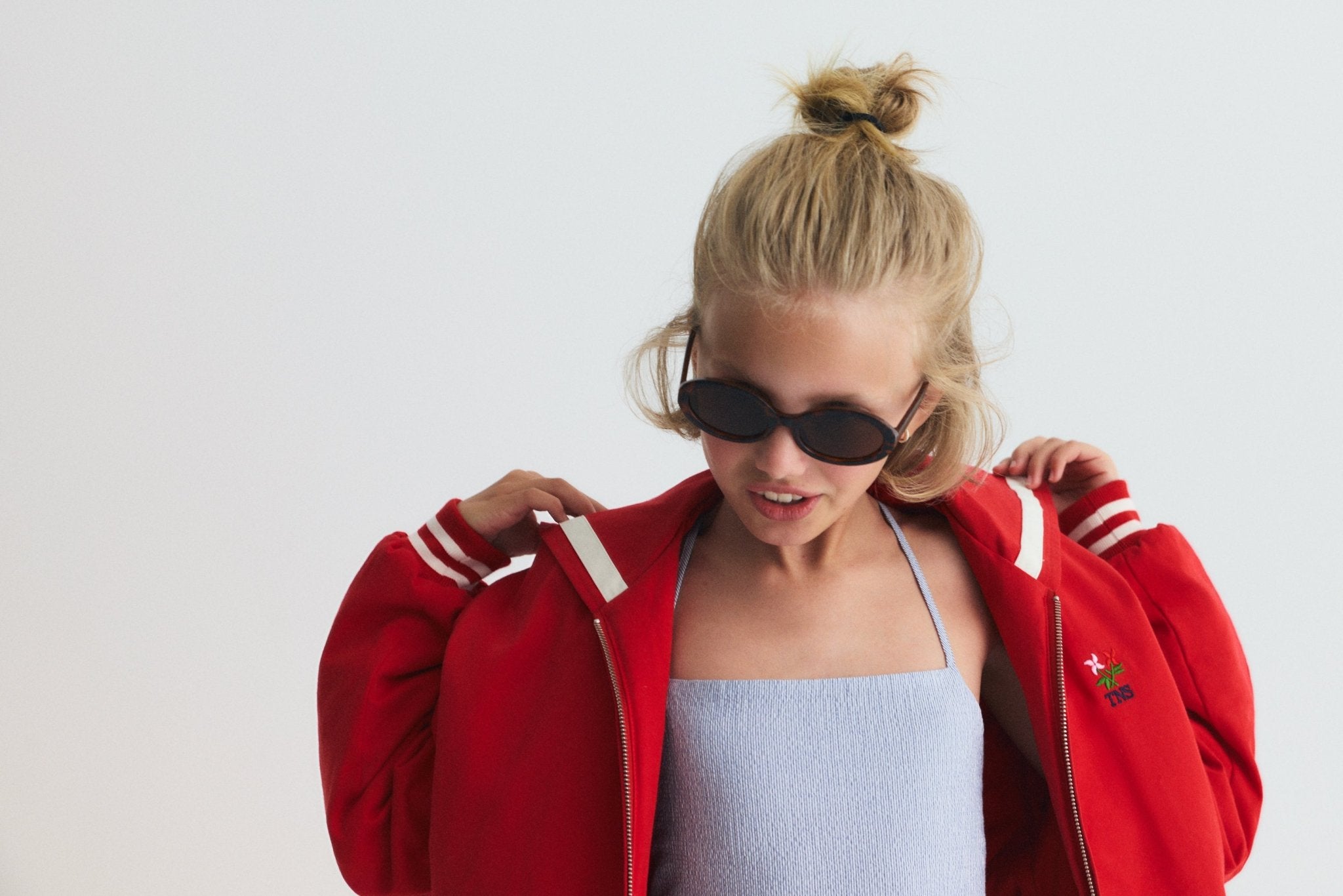 Chaqueta estilo bomber en un rojo vibrante, con un exclusivo cuello marinero, logotipo de la Sociedad bordado en la espalda y rayas en contraste. 