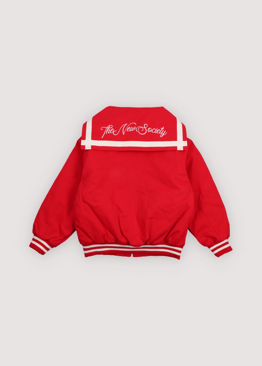 Chaqueta estilo bomber en un rojo vibrante, con un exclusivo cuello marinero, logotipo de la Sociedad bordado en la espalda y rayas en contraste. 