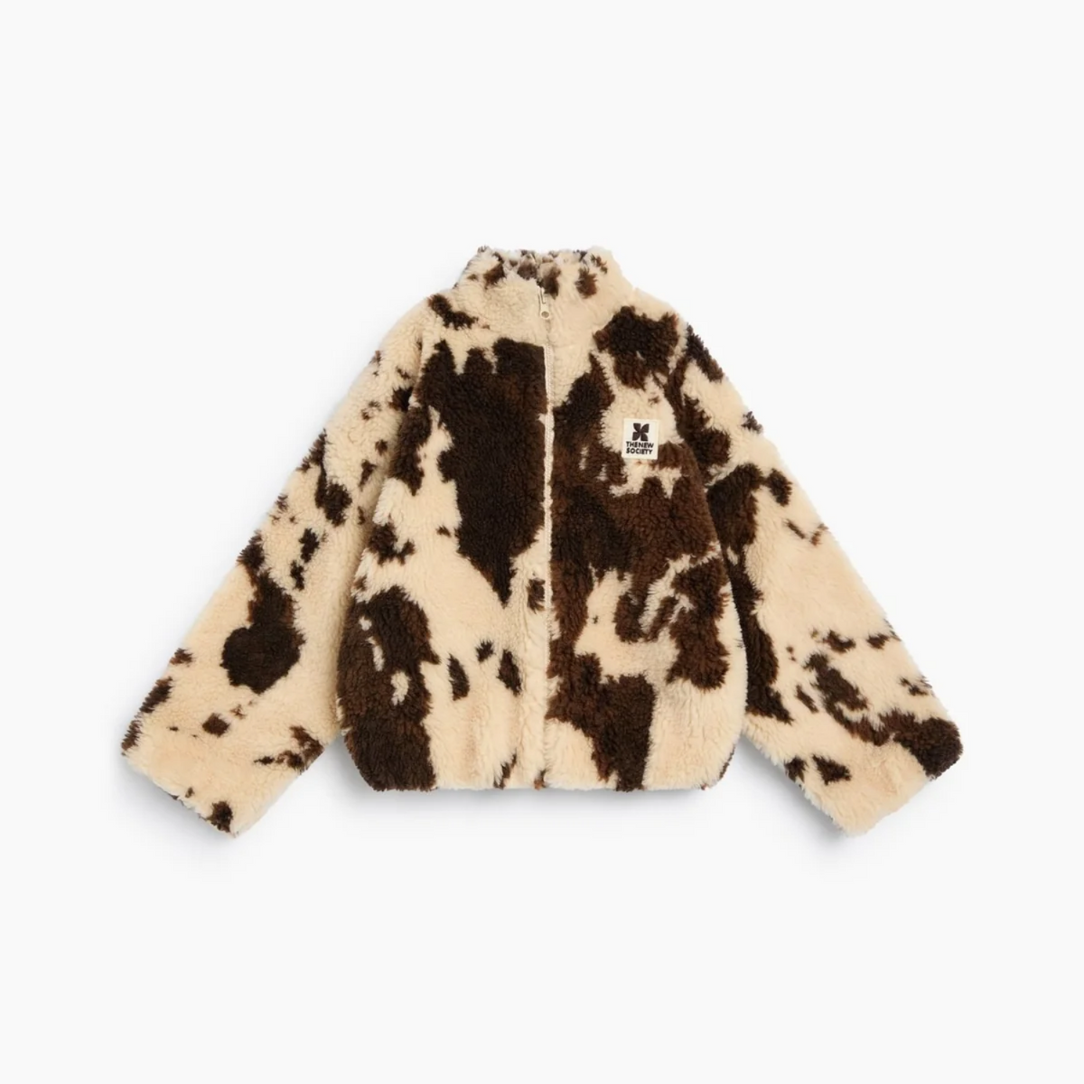 A cropped, long-sleeve fuzzy faux-fur jacket with a cow-print pattern in beige and dark brown, featuring a small black embroidered logo patch on the left chest, shown against a plain white background.