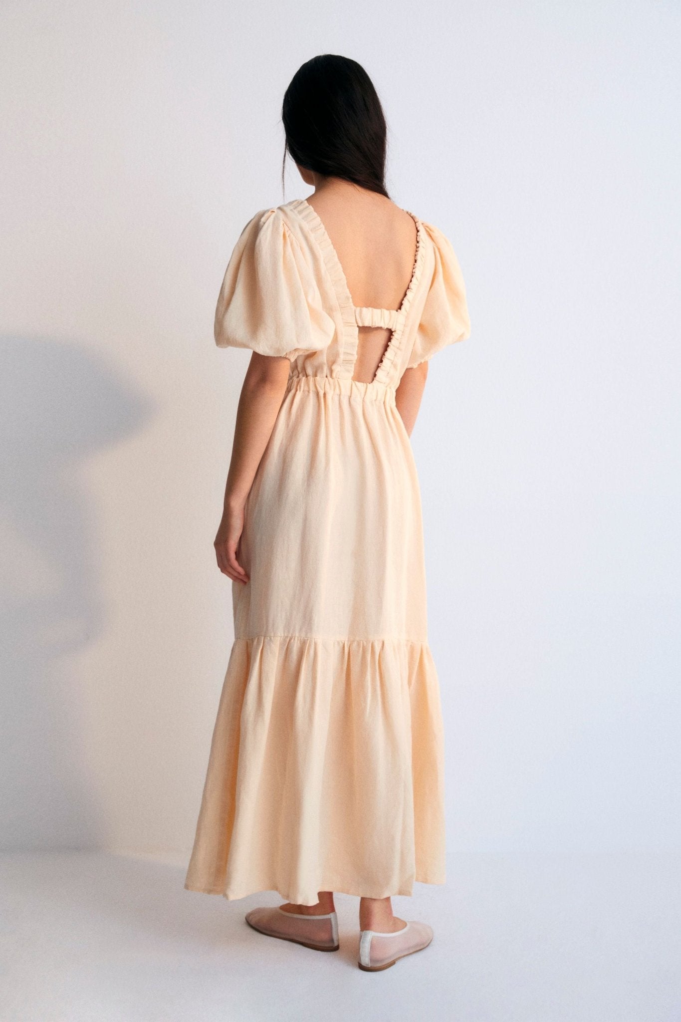 Hera Woman Dress 3 in 100% linen, available in two colors: caviar and macadamia. V-neck with elastic band, puffed sleeves, and an elastic waistband to generate volume in the skirt. Spring Summer Collection. The New Society.