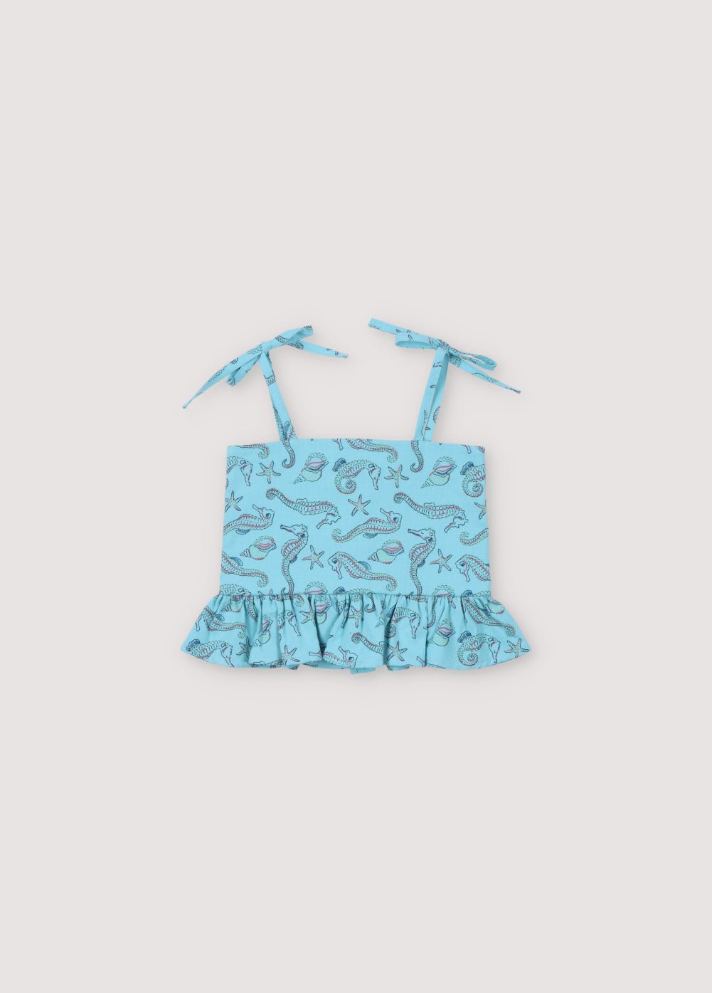 Haut bébé Io en tissu 100% coton avec notre imprimé hippocampes, caractérisé par un détail volant sur le bas, des boutons en nacre au dos et des bretelles. Collection printemps-été. The New Society.