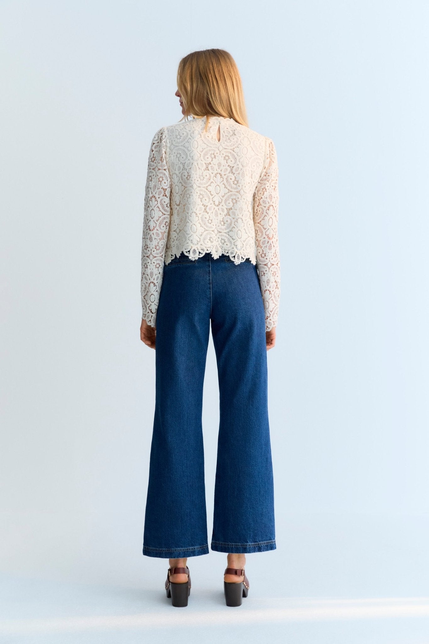 The Lara blouse is a very special crochet piece in off-white, featuring fitted sleeves with subtle volume at the shoulders and a back opening with a button closure.