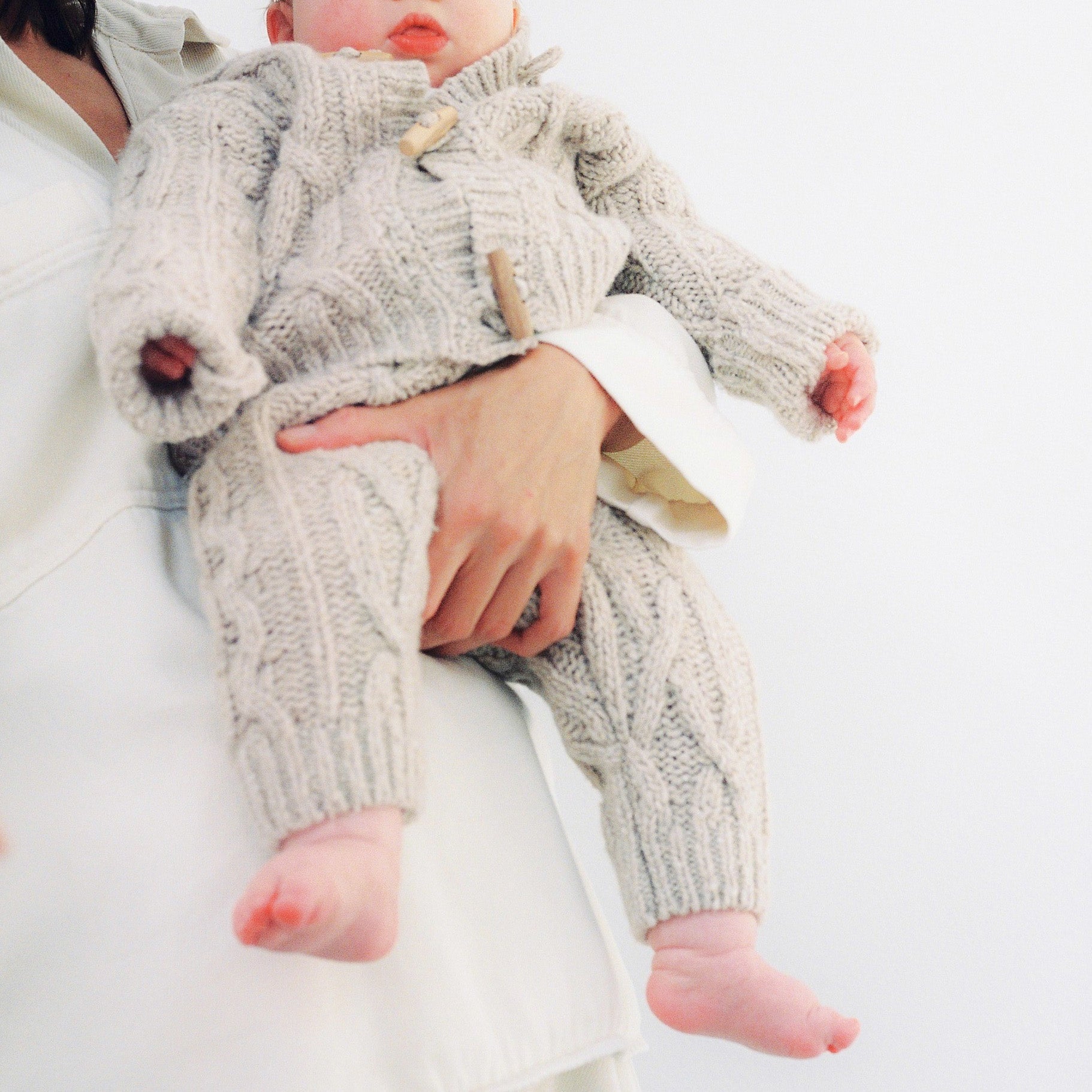 Knitted cardigan with a ribbed neckline, cuffs, and hem. Features a front opening with wooden toggles. Comes with matching knit pants to complete the look. Made with high-quality recycled materials.
