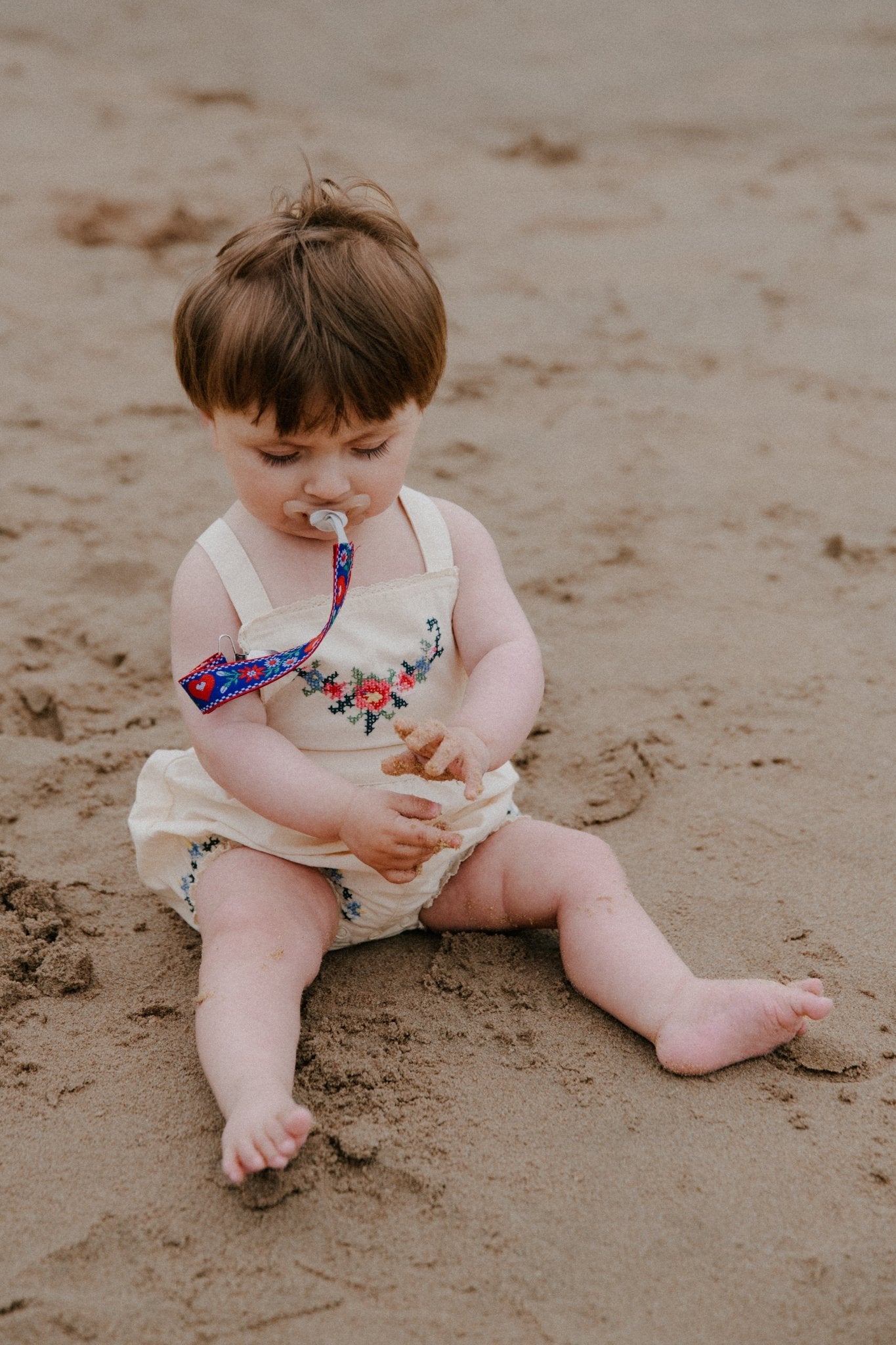 柔らかいコットン生地で作られたこのロンパースは、フロントと裾に細かく繊細な刺繍のディテールが施されています。