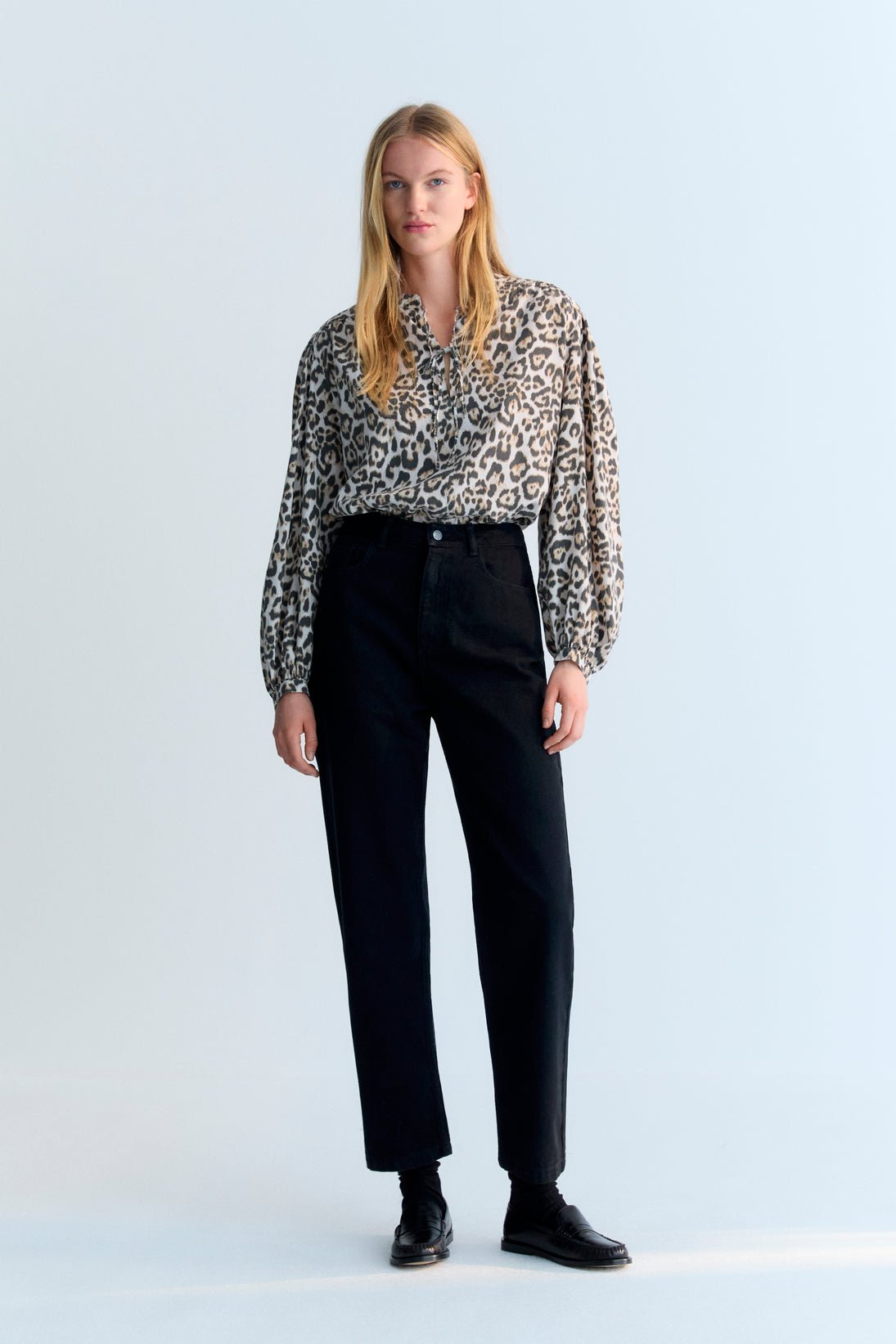 Woman wearing a patterned blouse and black pants on a white background