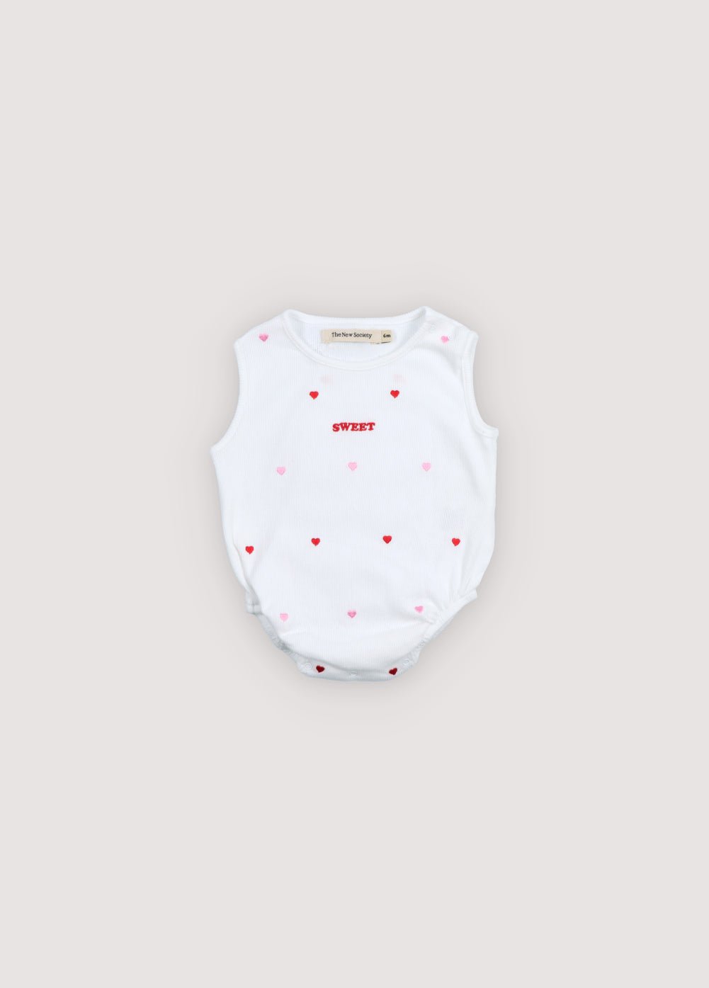 A soft cotton baby bodysuit featuring a delicate all-over heart print and a subtle logo detail on the front. 