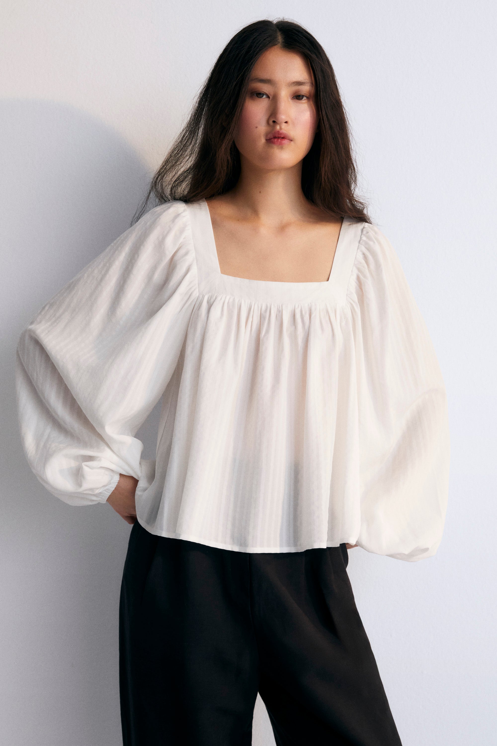 Blouse in crisp white is crafted from 100% Tencel striped fabric, offering a light and breathable feel. The square neckline adds a contemporary touch, while the gathered details create a flattering volume.