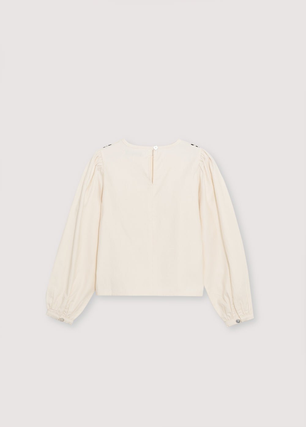 Blouse with a bust cut and gathering detail, featuring delicate contrast embroidery. It has a back opening with a tear and button closure.
