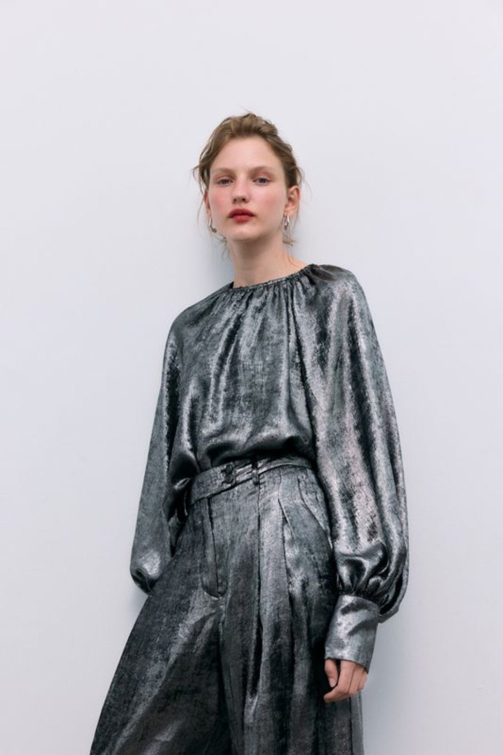 Silver shine blouse with a round neckline and gathered detailing, puffed sleeves with wide cuffs, and covered buttons in the same fabric. It features a back opening with a keyhole and button closure.